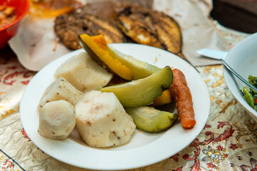 Traditional Indonesian meal with boiled vegetables, grilled fish, and side dishes
