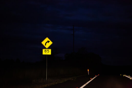 Sign on Golden Highway at night with arrow with 85 km/h recommended speed for turn