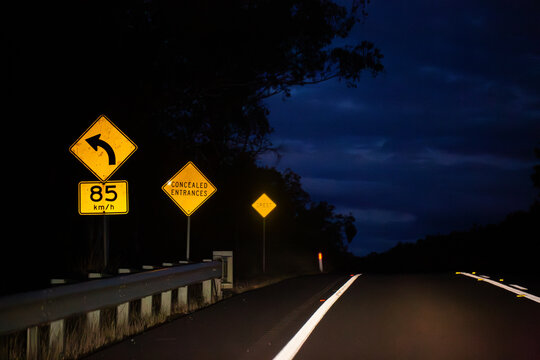 Sign on Golden Highway at night with arrow with 85 km/h recommended speed for turn