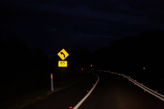 Sign on Golden Highway at night with arrow with 85 km/h recommended speed for turn