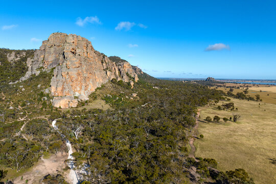 Rugged cliffs rising above woodlands and open plains under a clear blue sky