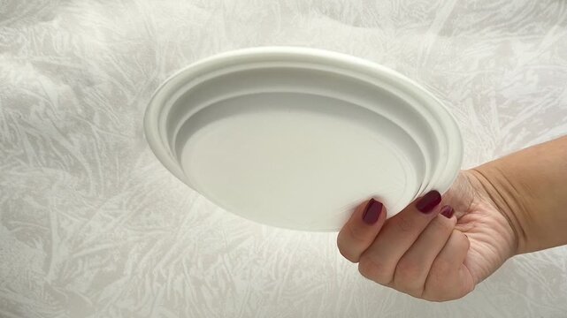 White disposable plastic plates in a woman's hand. The use of disposable tableware in public catering.