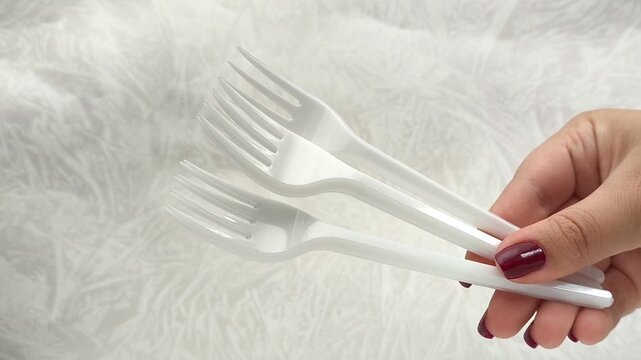 White disposable plastic forks in a woman's hand. The use of disposable tableware in public catering.