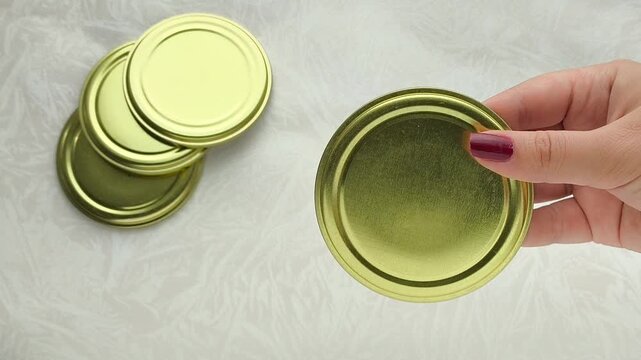 A gold metal lid for cans in a woman's hand, on the table are lids for turning with a key