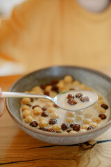 A person savors a bowl filled with colorful cereal and milk, sitting at a rustic wooden table. The setting suggests a cozy and relaxed breakfast atmosphere.