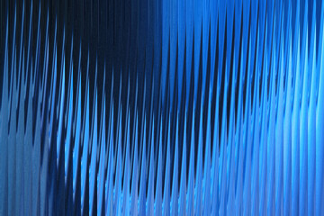 Abstract blue ribbed glass texture with dramatic lighting creating a sense of depth and movement © MDARMANKHAN