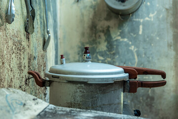 An Old alumunium pressure cooker with worn handles placed in a rustic kitchen, showing vintage cooking equipment against a weathered textured wall background