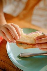 A young boy is holding a half-eaten sandwich with both hands, sitting at a table. He is engaged in a meal, possibly in a casual family setting, enjoying his food.