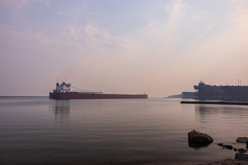 Fototapeta premium A Ship Leaving Ore Docks On Lake Superior During A Wildfire Smokey Hazy Evening