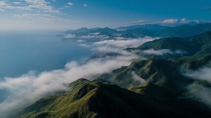 Breathtaking aerial view of majestic coastal mountains shrouded in ethereal mist and clouds, merging with the vast expanse of the tranquil ocean under a clear sky