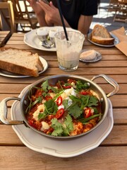 Shakshuka with herbs and chili served with bread on wooden table