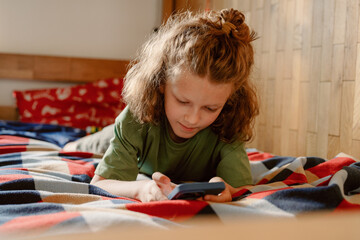 A young boy is laying on his bed, focused on a device in his hands. He enjoys moments of fun and connection with his father and brother throughout the day in a cozy room.