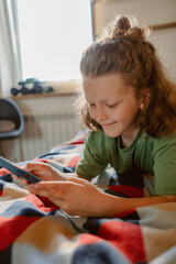 A boy relaxes on a colorful blanket while using his smartphone. He smiles as he engages with the device, showcasing a moment of leisure in a warm, inviting room during the day.