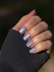 Close-up of Hand with Silver Cat Eye Magnet And Pink Shimmer Nail Polish. Nail Lacquer Swatch. Periwinkle Blue Magnetic Lacquer With Pink Shimmer And Silver Cat Eye Magnet On Fingers. Gray Long Sleeve