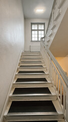 Bright and Clean Staircase with White Wooden Railing and Black Tread Strips, Leading Upward Toward a Window, Bathed in Soft Natural Light