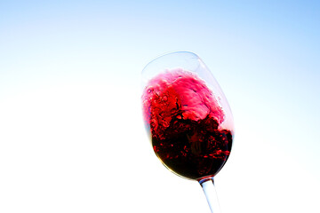 Red wine swirling on blue sky. Sommelier swirls with glass of red wine at sunset sky. Red Wine Swirling In Glass during vine Tasting, celebration vino party. Vibrant liquid splashing. Space for text