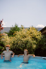Two boys relax together in a pool on a sunny day. They enjoy their time, interacting playfully and creating lasting memories in the backyard setting.