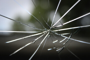 a close-up of broken glass, windshield or window, exhibiting a central point of impact with...