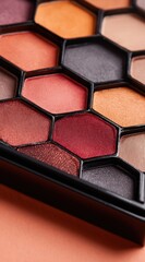 Fototapeta premium Close-up of a makeup palette featuring hexagonal compartments filled with various shades of eye shadow in warm, earthy tones on a peach background