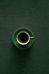 A coffee cup with saucer on a dark green textured background from above