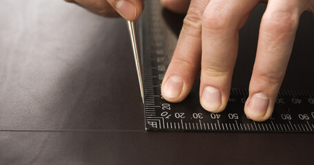 Close-up of craftsman marking leather with ruler and awl for handmade leatherwork