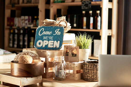 Interior of a store with natural products. Composition of shelves and boxes made of wood, homemade freshly-baked bread, a pot with flowers and a welcome sign on background of bottles with organic oil