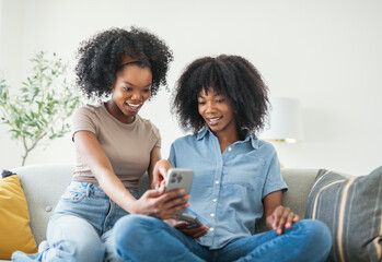 black mother and daughter using cellphone on sofa