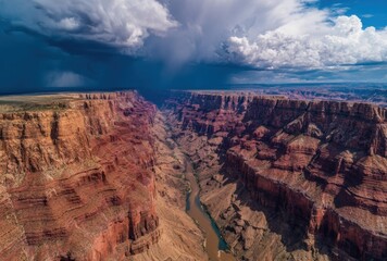 Dramatic aerial view of a massive canyon with layered red rock formations under a stormy sky and a winding river