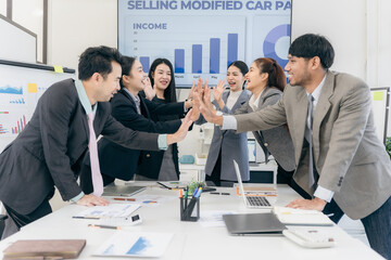 Group of happy Asian businesspeople congratulating each other to celebrate success in office conference room during meeting.