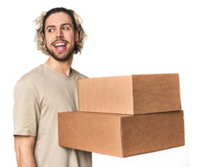 Young man with cardboard boxes in studio looks aside smiling, cheerful and pleasant.