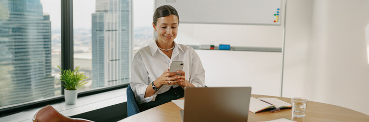 A professional woman is actively engaged with her mobile device while in the office environment