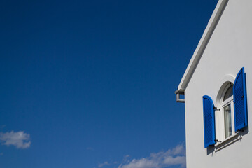 Minimalist White House With Blue Window Shutters And Clear Sky Background
