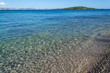 Obraz premium Transparent Pebble Shore and Crystal Clear Turquoise Sea With Blue Horizon on Summer Adriatic Coastline