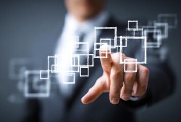 Man's hand in suit points to shimmering square patterns. Soft gray backdrop highlights glowing shapes creating a futuristic feel. Depth of field blurs the background