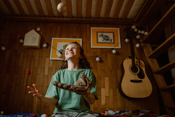 A young boy plays in his cozy room, smiling as he catches a baseball with his glove. Family photos and a guitar decorate the wooden walls, reflecting warmth and joy.