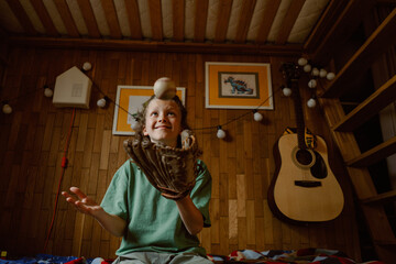 A boy enjoying a playful moment as he catches a baseball with his glove, smiling brightly in his warmly lit bedroom decorated with family photos and a guitar.