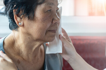 Elderly woman lying on sofa with caregiver applying an ice pack to her face, symbolizing family care, home healthcare, pain relief, swelling management, headache, and tooth problem treatment.