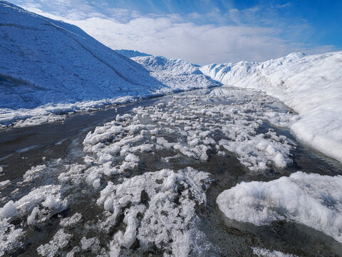 Ice chunks floating in glacial meltwater between snow-covered mountains under clear blue sky.