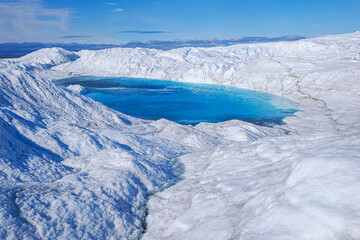 Vivid blue glacial meltwater lake amid white icy glacier terrain under a bright and clear sky.