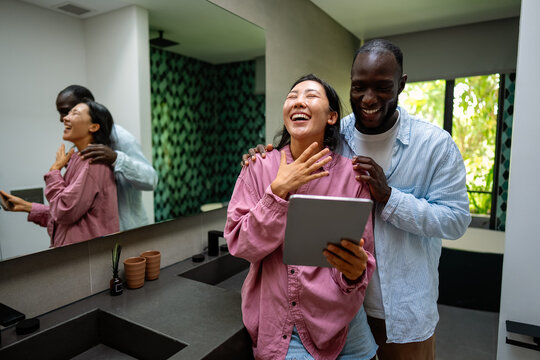 Happy young diverse, multiethnic couple planning budget, reading good news on digital tablet at home
