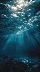 Sunbeams pierce deep ocean water, illuminating a dark, textured seabed.  Distant light creates a dramatic contrast