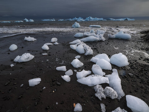 Ice chunks on black sand beach with dark ocean waves and dramatic sky, Disko Island, Greenland