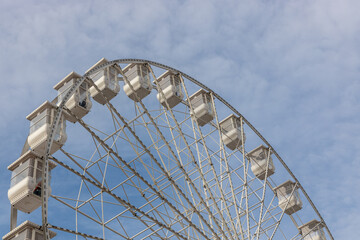 Large white Ferris wheel with passenger cabins. Amusement park attraction and symbol of summer vacation, leisure, and fun.