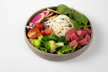 Noodles with tuna and vegetables in bowl on light surface
