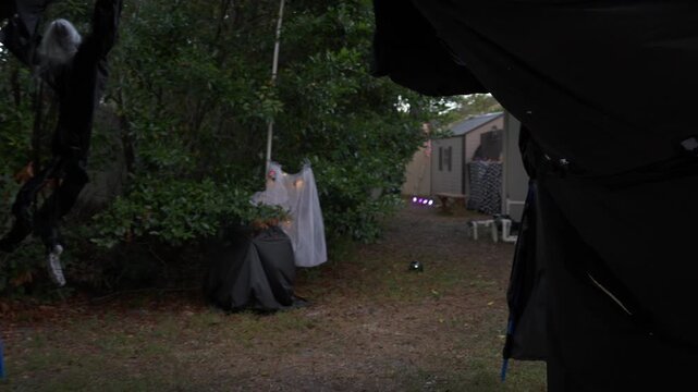 Backyard Halloween bar: skeleton bartender with skull decor, pumpkins, orange glow, and a jack-o-lantern near the shed.