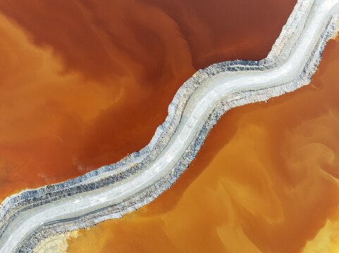 Fototapeta Track crossing a waste pond in the mineral-rich area of the Rio Tinto mines. The colour is caused by oxidised iron minerals. Aerial view. Drone shot. Huelva province, Andalusia, Spain