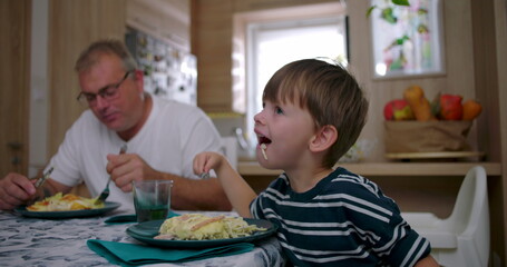 Father and son eating together at the table during a family meal, showcasing authentic connection...