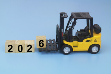 Yellow forklift truck arranging cubes with numbers 2026 on blue background. Symbol of new year coming.