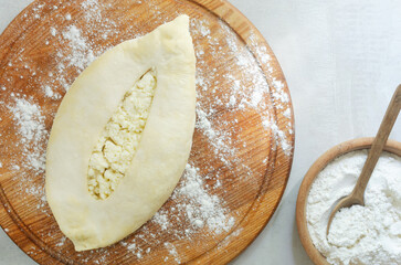 Khachapuri raw with scattered flour on a wooden cutting board. The process of making bread with cheese. The concept of traditional Georgian food. Horizontal orientation. Top view. Copy space