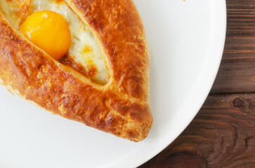 Adjarian khachapuri with egg yolk on a gray plate on a wooden table in the kitchen. The concept of traditional Georgian pastries. Horizontal orientation. Top view